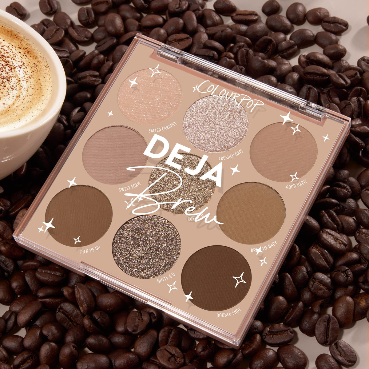 Deja Brew ColourPop Shadow Palette displaying nine coffee-inspired shades - matte and shimmer browns, taupes, and champagne - opened in a 3x3 layout on roasted coffee beans next to a latte, highlighting neutral eye looks.