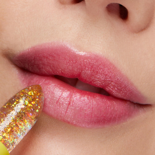 Thunderbolt ColourPop pH Lip Balm slicking onto lips, a clear jelly stick with gold iridescent flakes that reacts to pH to leave a glossy pink tint; close-up beauty shot showing hydrated, shiny finish.