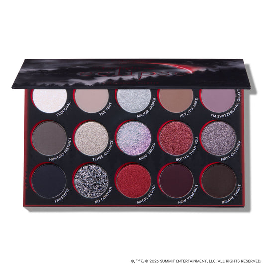 Eclipse shadow palette from the Twilight collection lying open, showing 15 circular pans of matte and glitter eyeshadows in silvers, reds, purples, and deep neutrals arranged in three rows inside a black and red themed case.