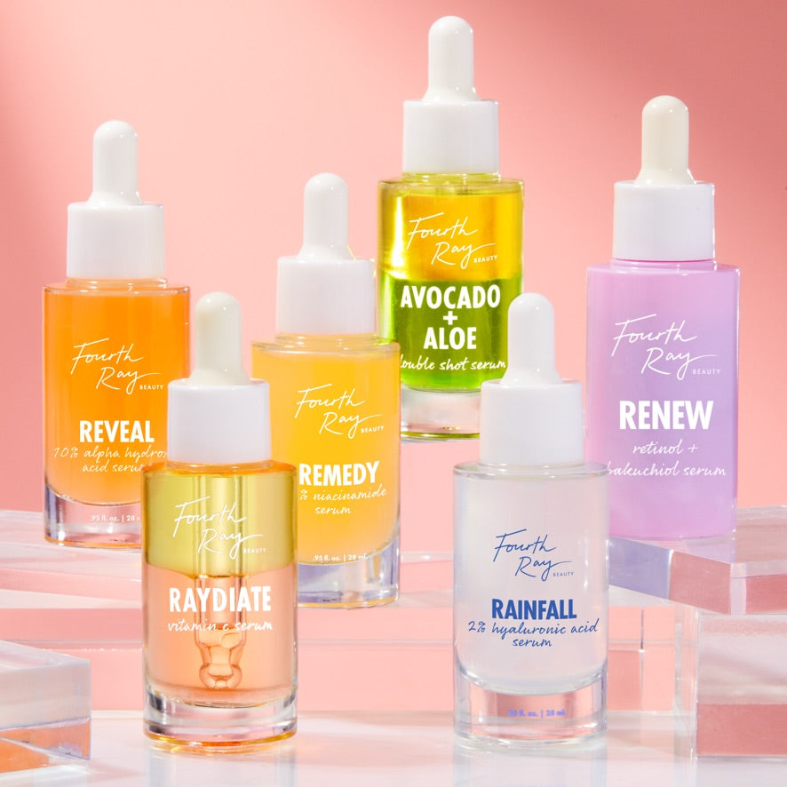 Reveal 10% AHA Serum bottle showcasing its label - orange-tinted glass with a white dropper - standing alongside other Fourth Ray Beauty treatments on clear acrylic risers against a pink gradient; exfoliating ColourPop Face Serum.