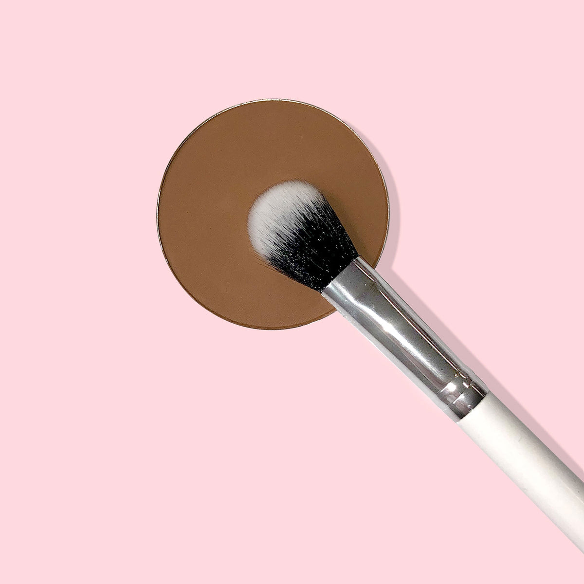 Small Fluff Brush makeup brush blending a brown round eyeshadow pan; dual‑tone black‑to‑white bristles, silver ferrule, and white handle on a pastel pink background, ideal for soft crease blending with ColourPop eyeshadows.