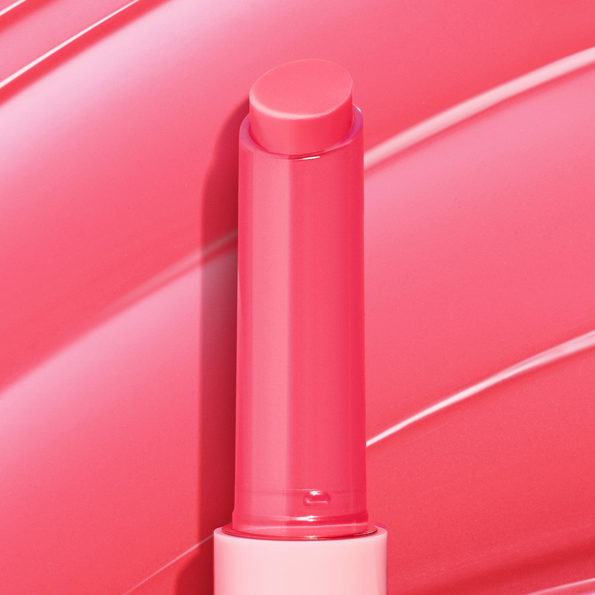Passenger Princess, a bright pink twist-up stick of ColourPop So Juicy Plumping Gloss Balm with Peptides, shown fully extended with a dewy sheen against a matching glossy swatch background highlighting its shiny, cushiony finish.