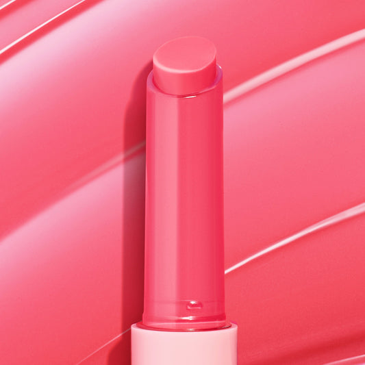 Passenger Princess, a bright pink twist-up stick of ColourPop So Juicy Plumping Gloss Balm with Peptides, shown fully extended with a dewy sheen against a matching glossy swatch background highlighting its shiny, cushiony finish.