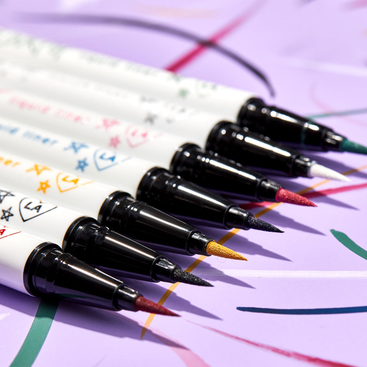 ColourPop BFF Liquid Liner in Crzy, a precision felt‑tip eyeliner, creating a crisp swipe; angled lineup of vibrant colored tips beside it on a lavender background with playful swatch lines.