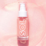 ColourPop SOL Shimmering Dry Oil in Pink Champagne stands upright with a pump and clear cap, showcasing rose-pink, gold-flecked oil in a glass bottle labeled SOL against a luminous pink glitter background.