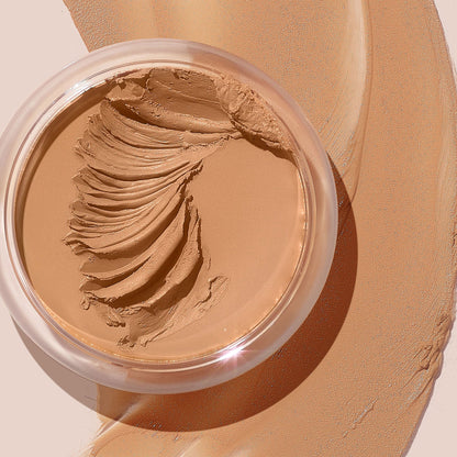 ColourPop SOL Face & Body Bronzing Balm in shade Light sits in a clear round jar with creamy swirls, with warm golden-tan balm swatched around it on a beige surface, showcasing a smooth, blendable texture and natural dewy finish.