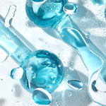Cooling Facial Globes glisten as blue glass spheres with handles roll among water droplets on a clear surface, highlighting a chilled de-puffing facial massage tool set from ColourPop Skincare Tools And Accessories.