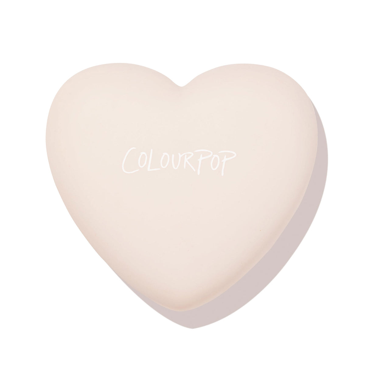 Heart-shaped ColourPop Kiss 'N Tell pressed powder blush compact rests closed, showcasing a soft beige lid with white ColourPop logo on a clean white background.