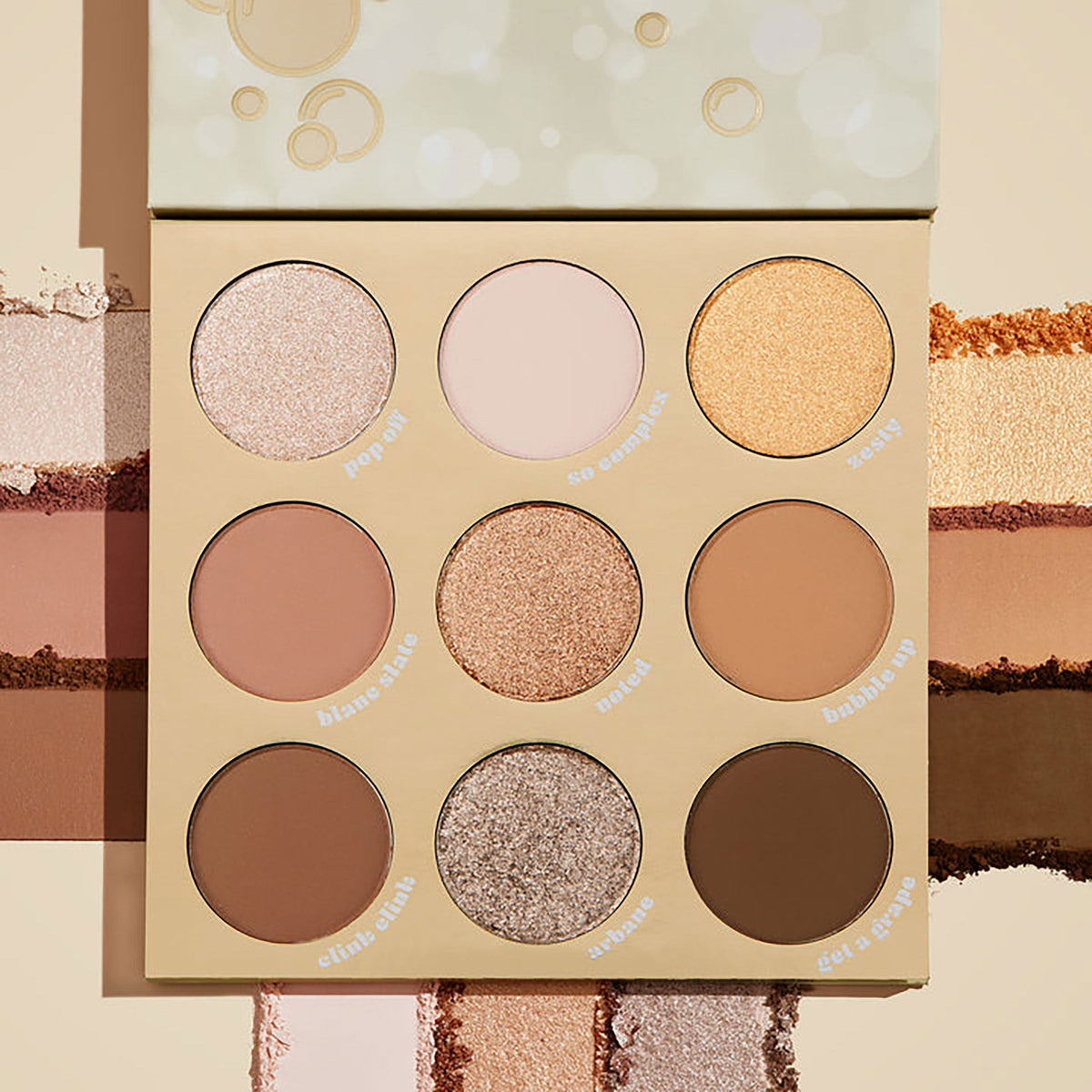 ColourPop Feelin' Bubbly shadow palette open, showing a 9-pan range of champagne, gold, taupe, and brown shades in matte and shimmer finishes, set on a cream backdrop with pigment swatches and bubbly-themed beige packaging.