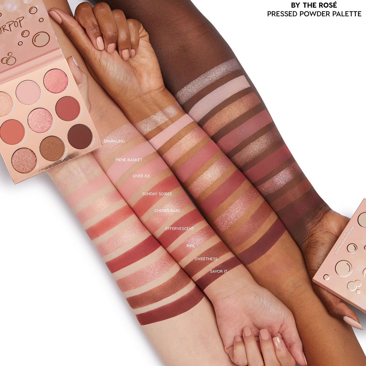 By The Rosé 9-pan pressed‑powder ColourPop Shadow Palette shown open with rose, mauve, and bronze mattes and shimmers, with swatches across three arms in light, medium, and deep skin tones to show payoff; blush‑pink packaging on white.