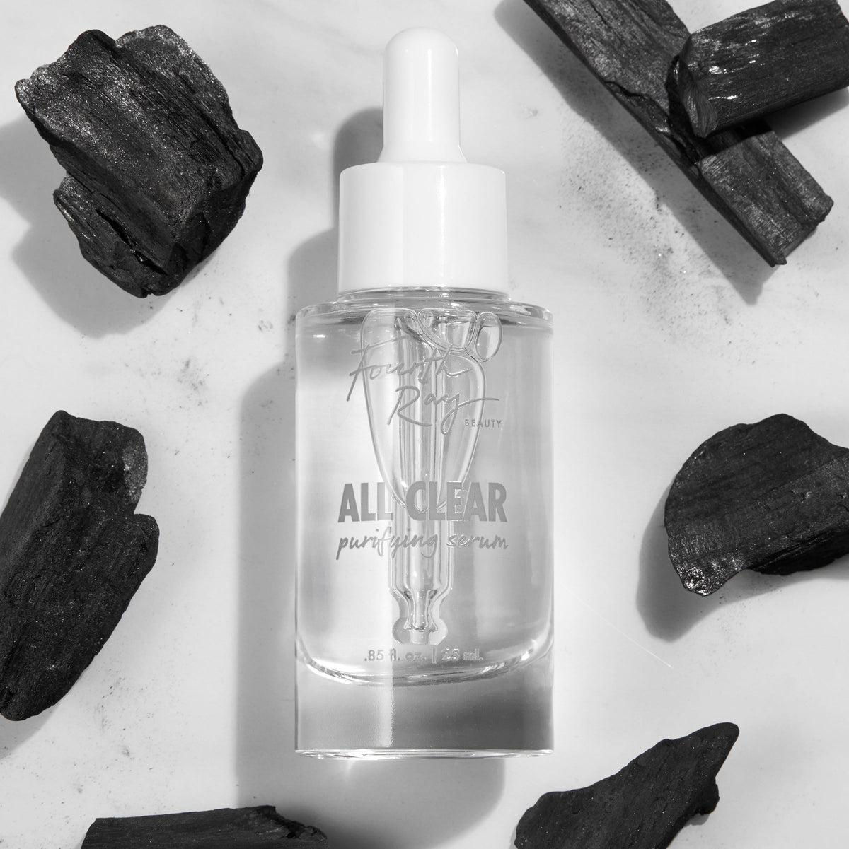 Glass dropper bottle of Fourth Ray Beauty All Clear Purifying Serum standing upright, showcasing clear formula and label, surrounded by charcoal pieces on a white marble surface; .85 fl oz/25 mL ColourPop Face Serum for purifying skin.