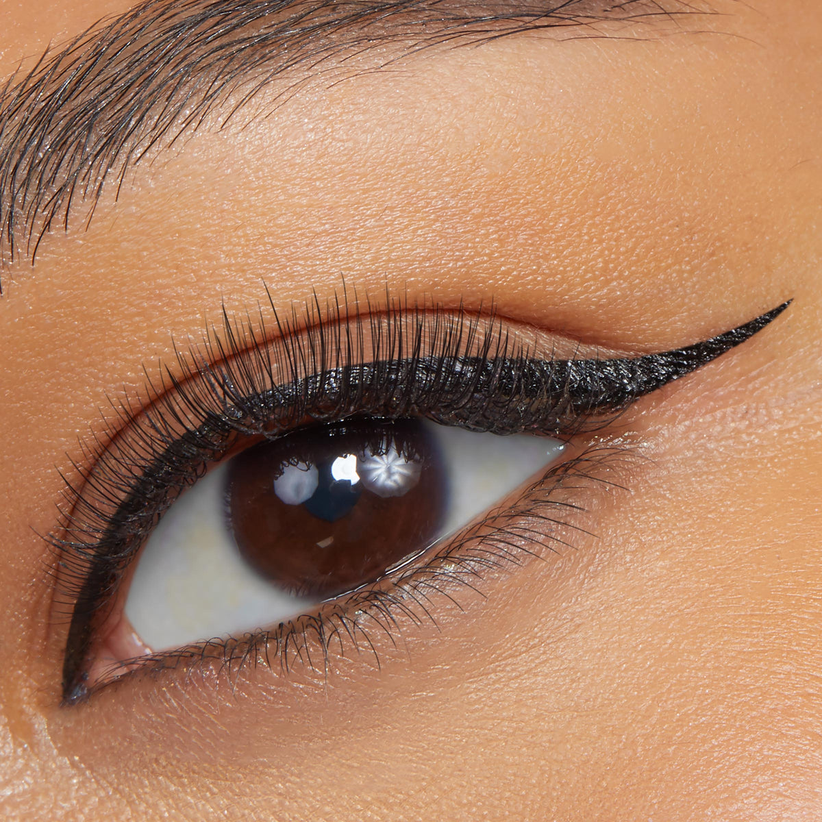 Sharp black cat-eye wing defining the upper lash line, applied with ColourPop BFF Liquid Liner in Numero Uno, on a close-up brown eye with natural lashes and smooth skin.