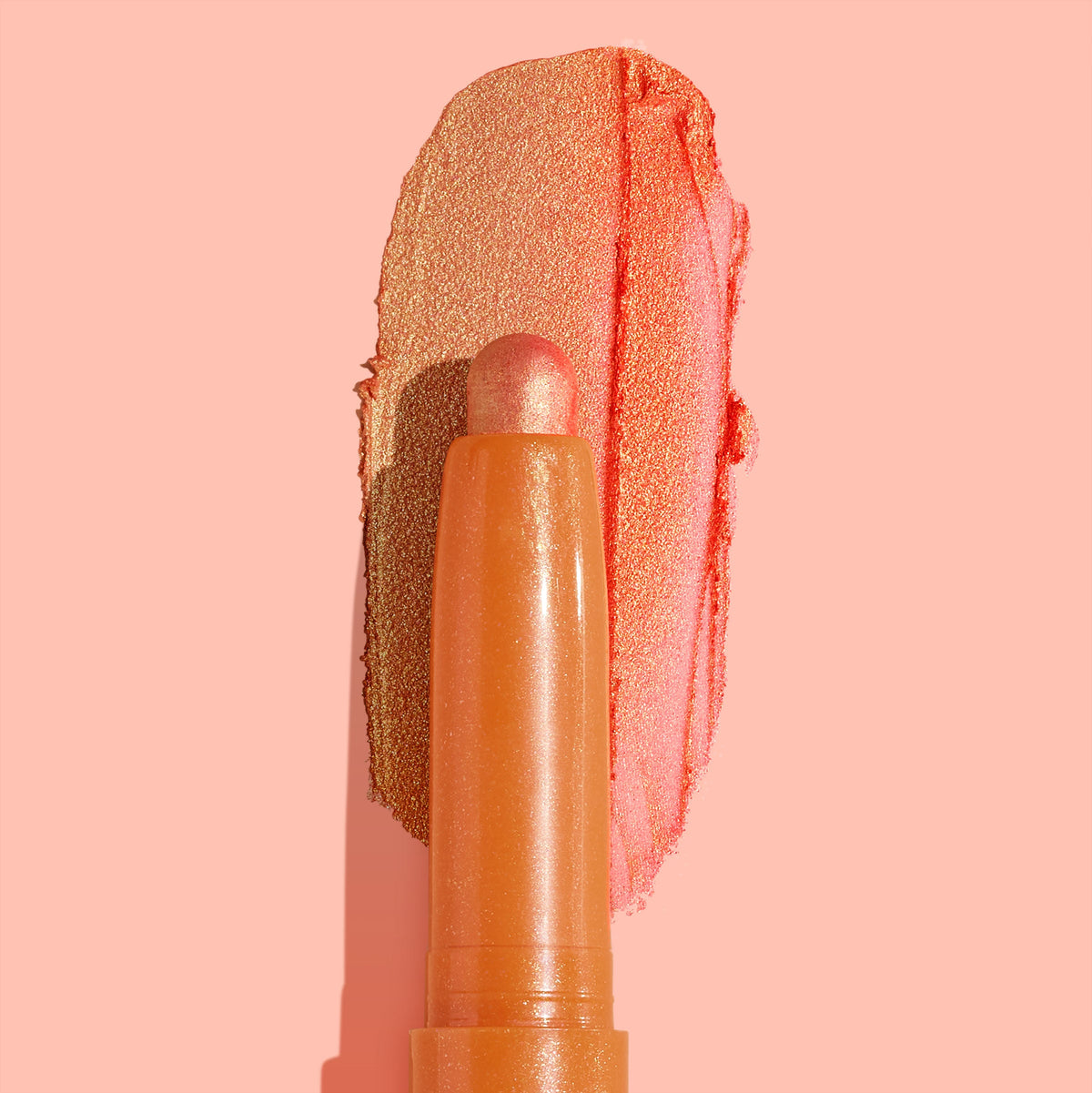 ColourPop Shadow Stix Friday Feels glides a metallic peach-coral swipe across a blush-pink background, showcasing the creamy twist-up eyeshadow crayon and its shimmery finish.
