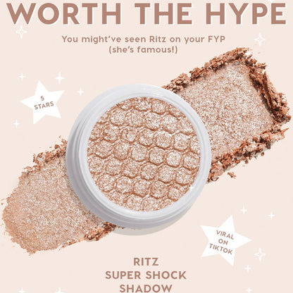 ColourPop Ritz Super Shock Shadow single, a metallic champagne‑taupe eyeshadow with silvery sparkle, shown in an open white pot with honeycomb texture as crushed pigment swipes across a nude backdrop with star graphics and hype callouts.