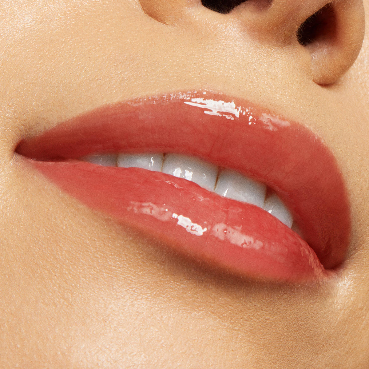 Glossy, coral-pink lips wearing Vampy Lips Lux Lip Oil, showcasing a sheer, high-shine finish from ColourPop Lux Lip Oil as the mouth softly smiles with teeth peeking, close-up on smooth, hydrated skin.