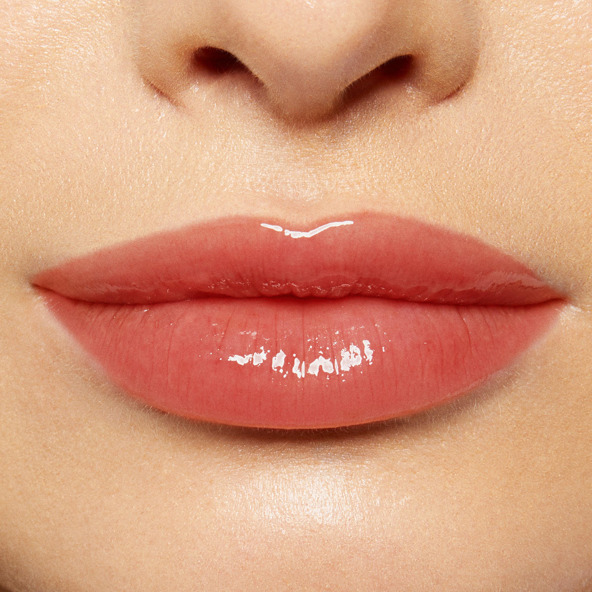 Glossy lips wearing ColourPop Lux Lip Oil in Bells, delivering a sheer peachy-rose tint and glass-like shine; smooth, non-sticky finish shown in a tight close-up of the lower face under soft studio lighting.