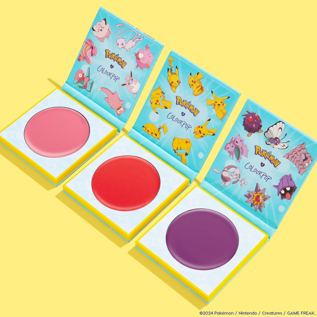 ElectroBall ColourPop Cream Blush trio opened to reveal pink, red, and purple pans, teal lids printed with Pikachu and other Pokémon, arranged in a flat lay on a bright yellow background.