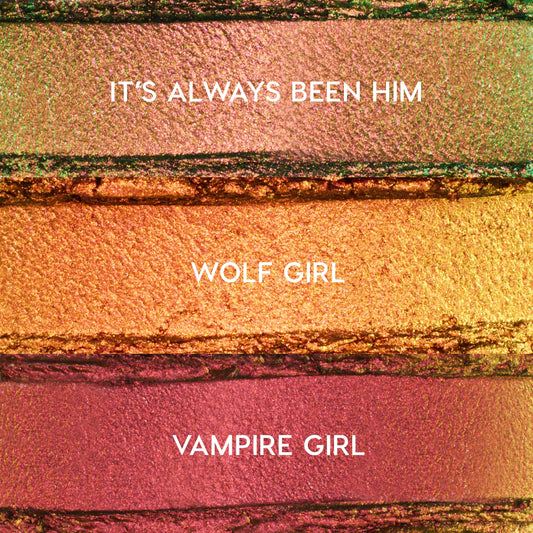 ColourPop Shadow Stix Love Triangle bundle swatches showing three metallic shades - It’s Always Been Him (pink‑green duochrome), Wolf Girl (copper gold), and Vampire Girl (rosy plum) - spread in horizontal strips on a textured makeup surface.