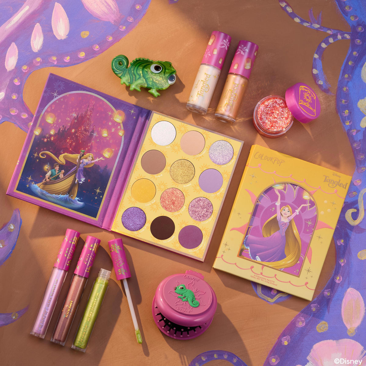 Disney Tangled and ColourPop Collection full makeup set laid flat, featuring Rapunzel-themed eyeshadow palette, lip glosses, glitter, and green chameleon accessory on a purple-and-gold illustrated background promoting ColourPop back in stock collection.