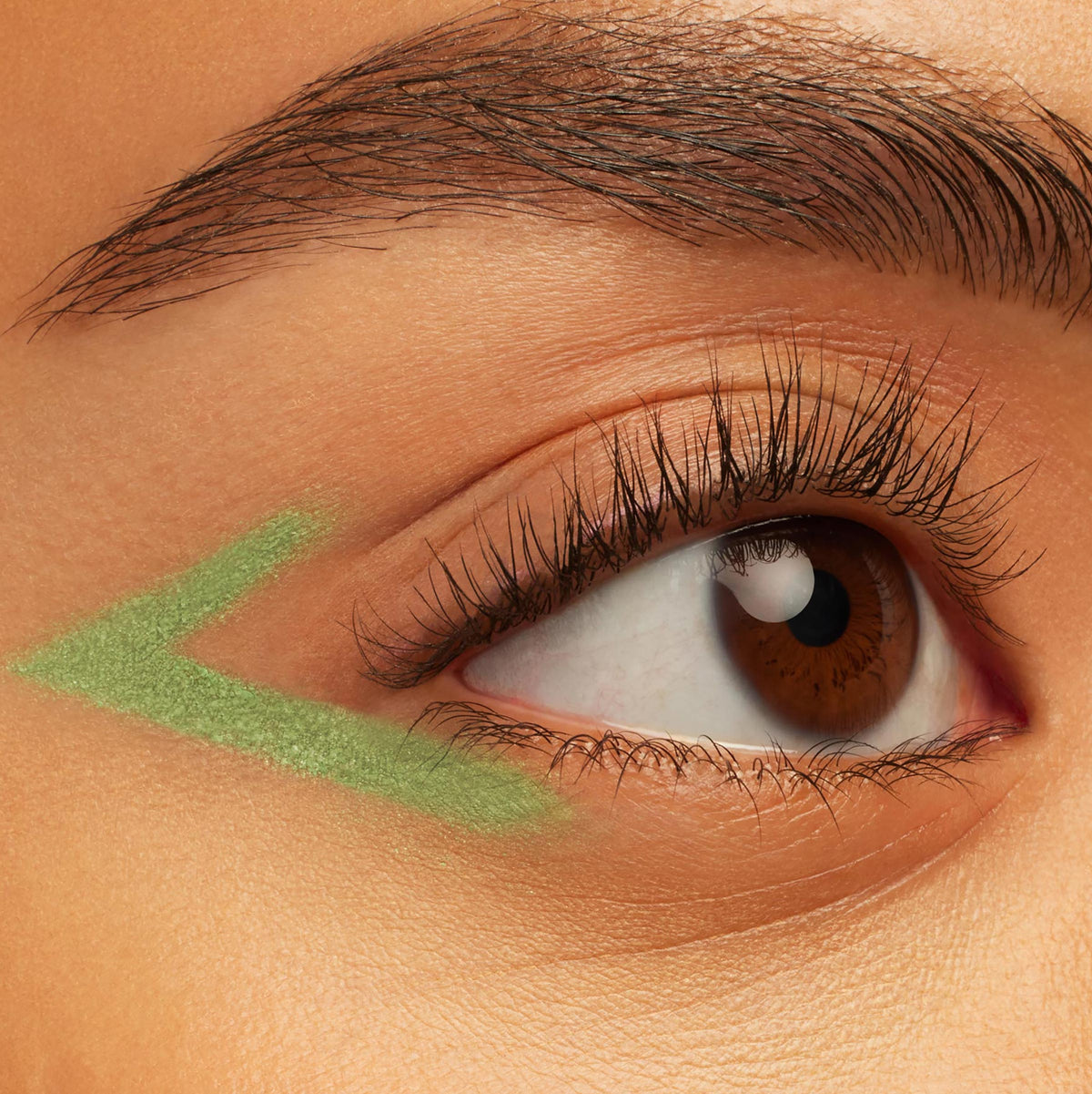 ColourPop Aglow Crème Gel Liner draws a shimmery pastel green V-shaped wing under the outer corner of a brown eye, showing creamy payoff and precise glide in a close-up beauty shot.