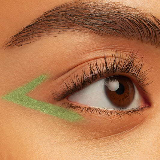 ColourPop Aglow Crème Gel Liner draws a shimmery pastel green V-shaped wing under the outer corner of a brown eye, showing creamy payoff and precise glide in a close-up beauty shot.
