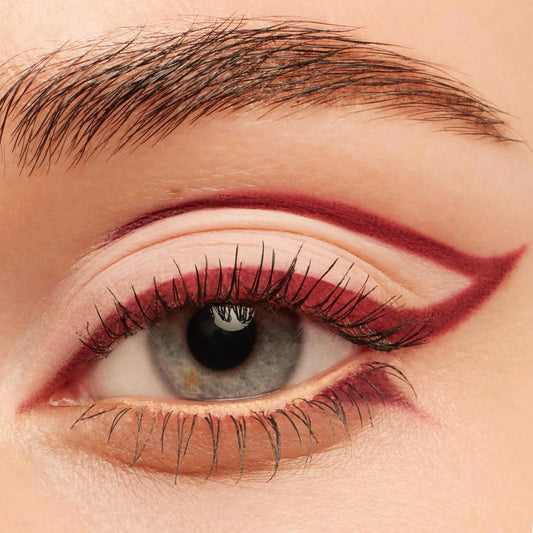 Burgundy graphic winged liner framing a gray-blue eye, created with Joy Ride, ColourPop Crème Gel Liner, tracing the upper crease and lower lash line with a sharp extended flick for a bold, precise look.