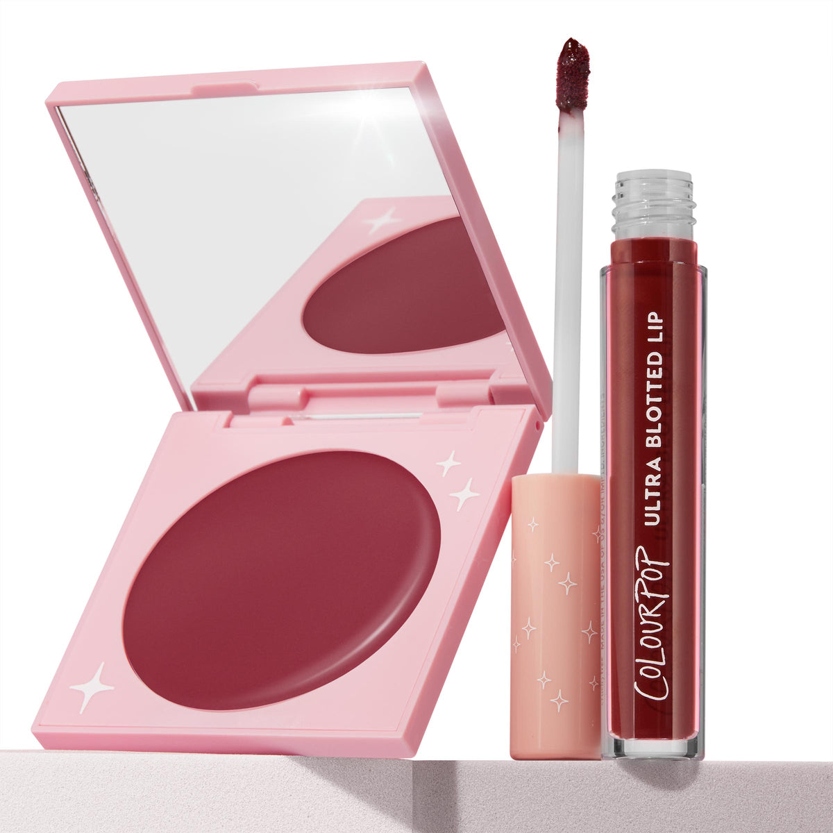 Blush n' Pout ColourPop Cheek & Lip Set showcasing a pink mirrored compact with deep berry cream blush open beside an Ultra Blotted Lip tint, doe-foot applicator lifted from the clear tube; star-studded pink packaging on a minimal light surface.
