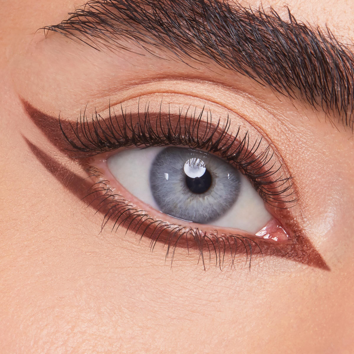 ColourPop Crème Gel Liner Sunnyvale tracing a sharp rich-brown double wing on a blue eye - lining upper and lower lashes with a pointed inner corner - over nude shadow, showcasing precise, long-wear crème gel eyeliner for graphic looks.