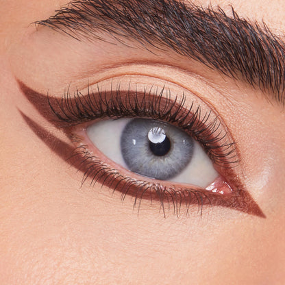 ColourPop Crème Gel Liner Sunnyvale tracing a sharp rich-brown double wing on a blue eye - lining upper and lower lashes with a pointed inner corner - over nude shadow, showcasing precise, long-wear crème gel eyeliner for graphic looks.