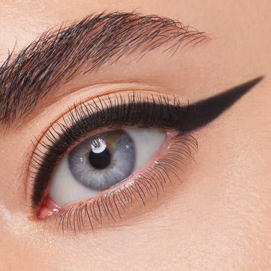 ColourPop Crème Gel Liner in Swerve draws a jet-black, precise cat-eye wing across the upper lash line of a blue eye, showcasing smooth, matte payoff and long-wear definition in a close-up beauty shot.