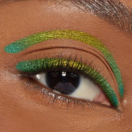 Wild Idea ColourPop Chrome Crème Gel Liner traces a metallic lime‑to‑teal wing along the upper lash line and a bold floating crease stroke above it on a brown eye, macro beauty shot highlighting the chrome finish and precise graphic look.