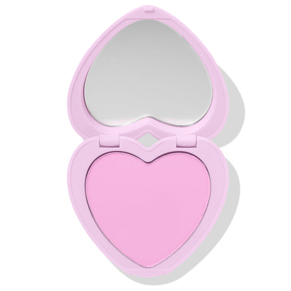 Cupid’s Bow ColourPop Pressed Powder Blush sits open, showcasing a baby‑pink heart‑shaped pan and built‑in mirror in a pastel lavender heart compact on a white backdrop.