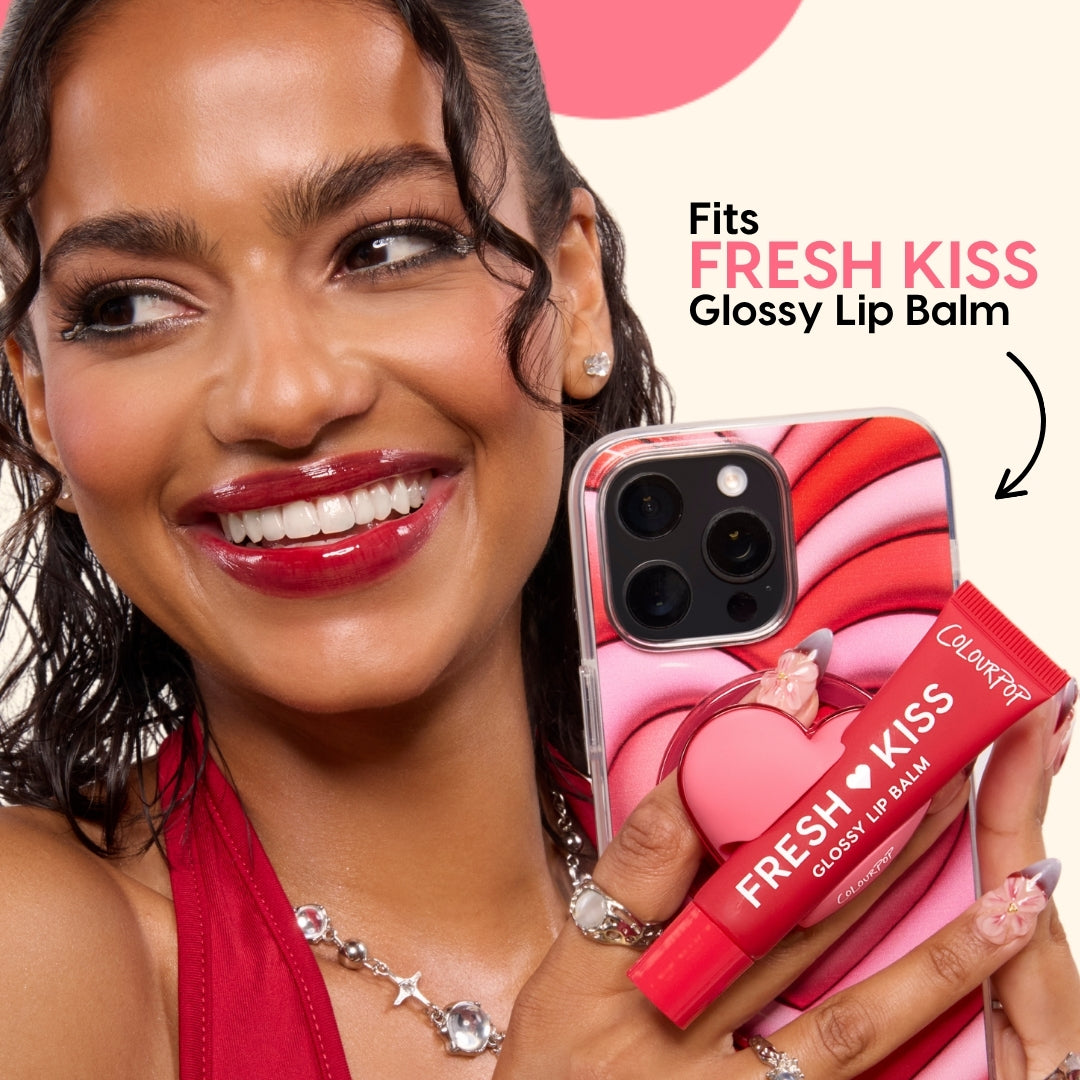Smiling woman holds a phone with a pink ColourPop ColourPopSockets heart grip and matching Fresh Kiss glossy lip balm, showcasing the red lip stain accessory as a fun Colourpop beauty tool in the Brushes & Tools category.