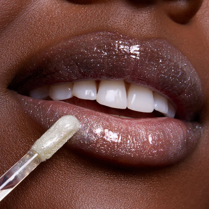 Close-up lips wearing Bright Ariel Ultra Glossy Lip, a shimmering Disney Princess lip gloss applied with a doe-foot applicator, showing sparkling high-shine finish on deep skin for a glamorous makeup look.