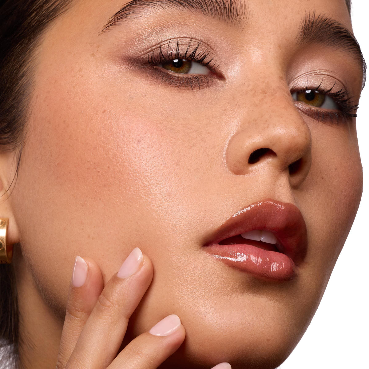 Glossed lips wearing ColourPop So Juicy Plumping Gloss Balm with Peptides, shade Perfection, delivering a plumped high-shine finish as a model touches her cheek; close-up beauty shot with neutral eyeshadow in studio lighting.