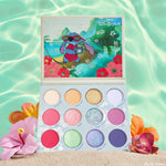 Beach Dreamin' ColourPop Shadow Palette opens to 12 tropical mattes and shimmers - coral, peach, gold, icy white, pink, mint, aqua, lilac, and deep violet - with Disney Lilo & Stitch art on the lid, set on sand with hibiscus and pool-blue water.