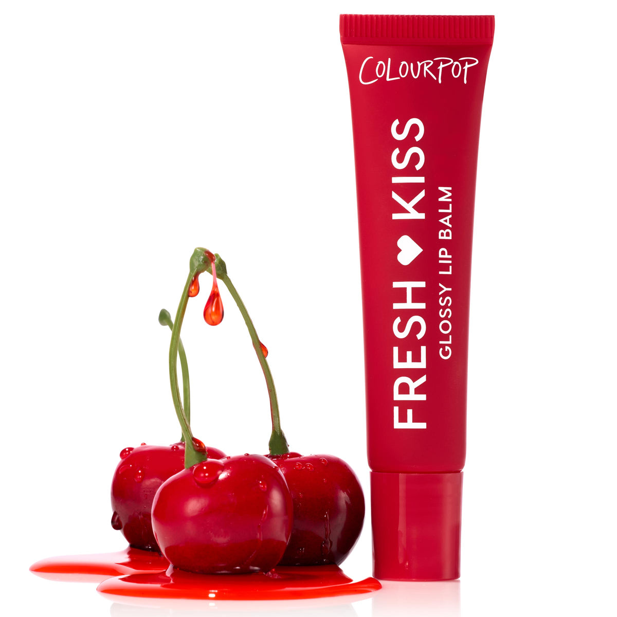 Cherry Glaze ColourPop Fresh Kiss Glossy Balm tube stands upright with “Fresh Kiss Glossy Lip Balm” branding, beside glossy cherries dripping red syrup into a puddle on a stark white background.