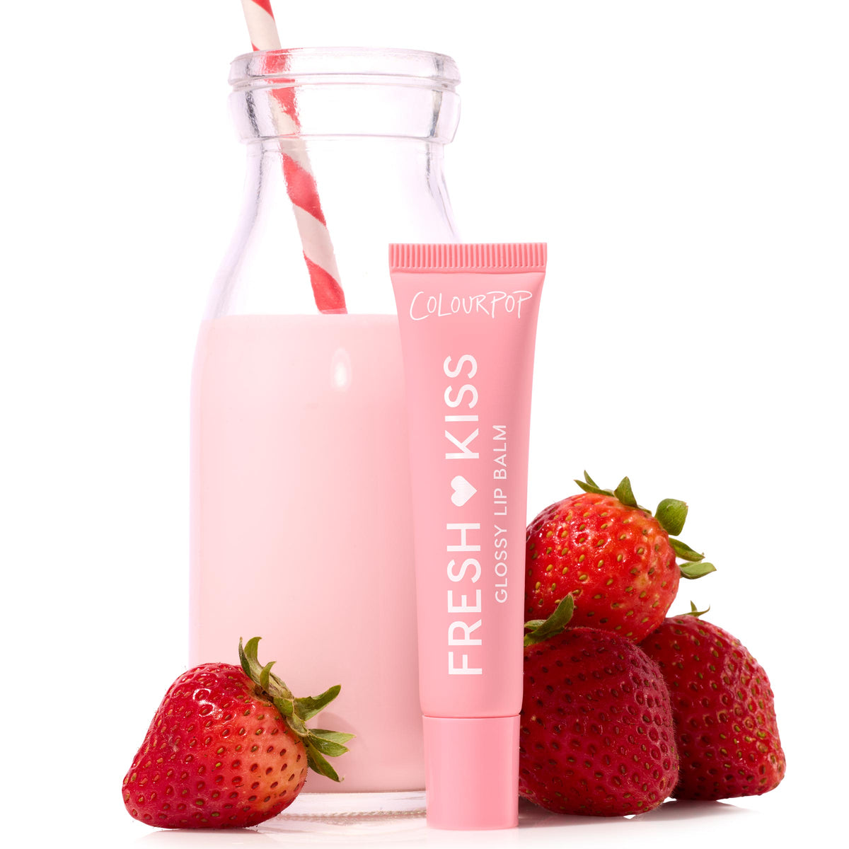 ColourPop Fresh Kiss Glossy Balm, shade Strawberry Milk, stands in a pink squeeze tube beside a glass bottle of strawberry milk with a red-and-white straw and fresh strawberries on a white backdrop.