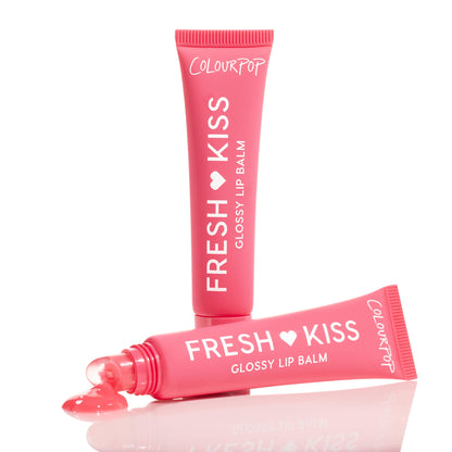 ColourPop Fresh Kiss Glossy Balm in Watermelon Sugar, one tube standing and another squeezed to reveal a shiny coral-pink dollop on a reflective white surface, showcasing the hydrating lip balm in bright pink packaging with white lettering.