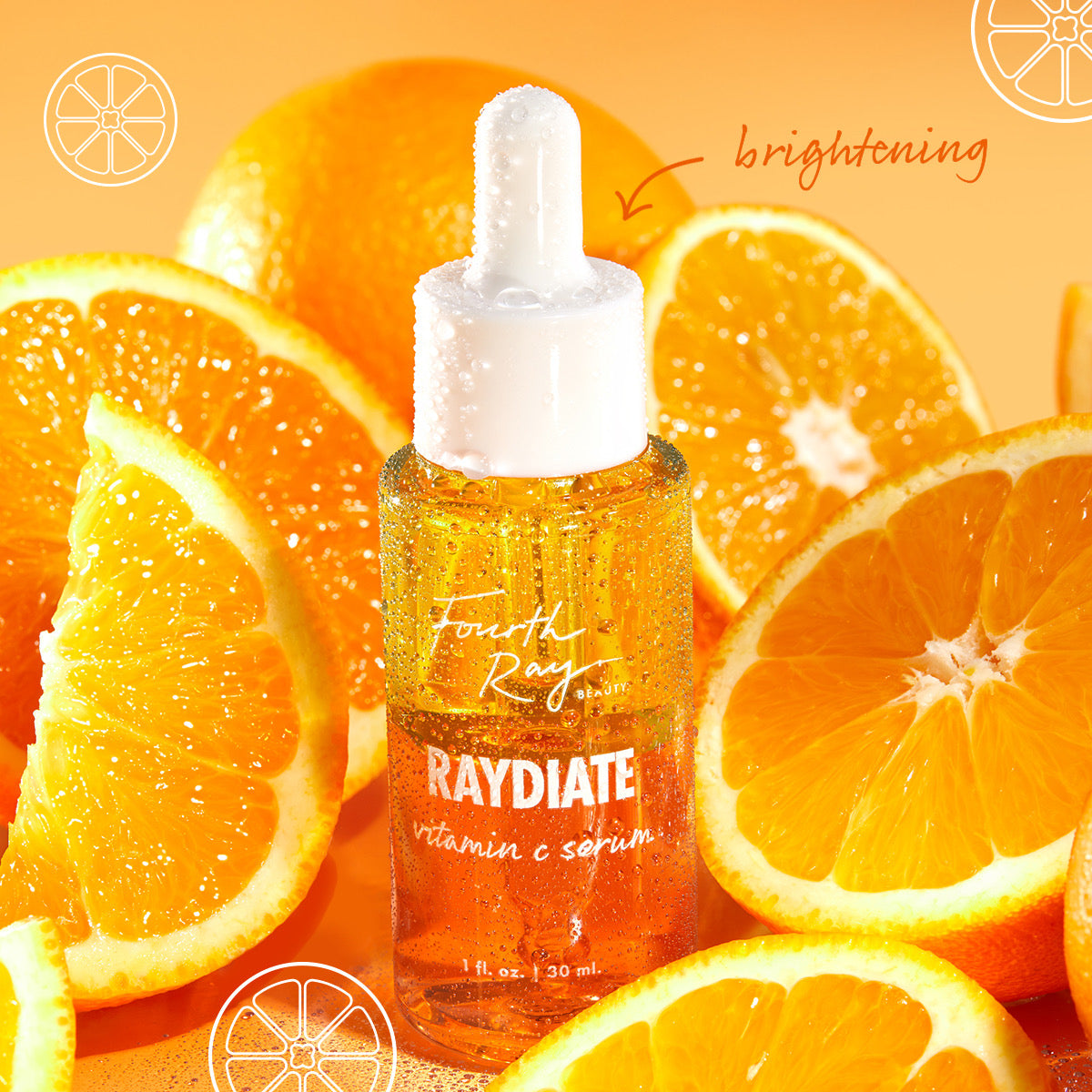 Fourth Ray Beauty Raydiate Vitamin C Serum 1 fl oz dropper bottle glistens with dew among fresh orange slices on a bright citrus background, highlighting brightening in the Get That Glow ColourPop Face Set.