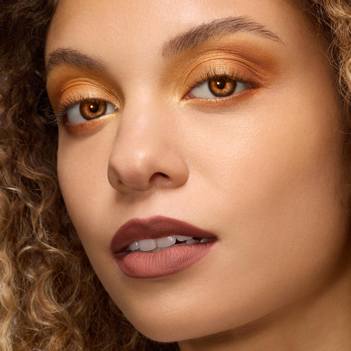 Model showcasing Twilight New Moon x ColourPop Full Collection with shimmering amber‑gold eyeshadow, warm copper lower lash line, and matte cocoa‑brown lipstick in a studio close‑up, highlighting pigments from the ColourPop Full Collection Set.