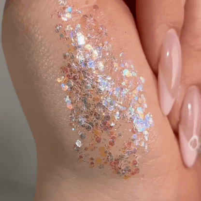 Disco Lady ColourPop Glitter Gel swatched on the back of a hand, shimmering with multicolor iridescent hex and micro-glitter in a clear gel base, catching light beside glossy nude-pink nails in a tight beauty close-up.