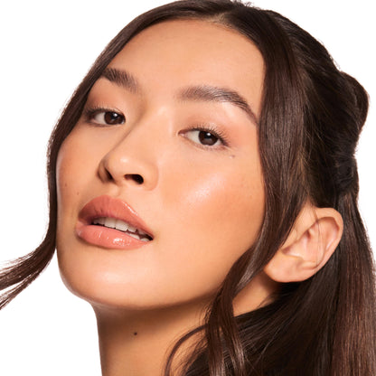 Close-up glossy nude lips, model tilting head to show Sweet Treats, a ColourPop Glossy Lip Balm Trio, delivering caramel latte shine with dewy skin and soft makeup against a clean white background.