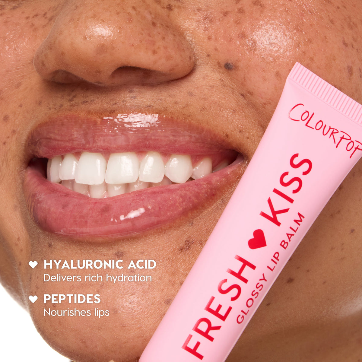 Smiling glossy lips wearing balm, holding a pink tube labeled ColourPop Fresh Kiss Glossy Lip Balm; close-up freckled skin; callouts mention hyaluronic acid for rich hydration and peptides that nourish lips.