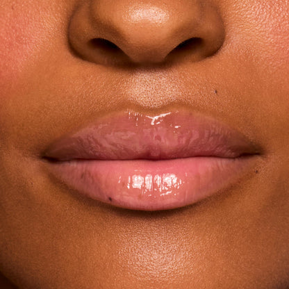 Glossed lips wearing ColourPop Fresh Kiss Glossy Balm in Strawberry Milk, delivering a sheer milky pink tint with a high-shine, glassy finish; macro close-up on smooth skin for a natural everyday lip look.