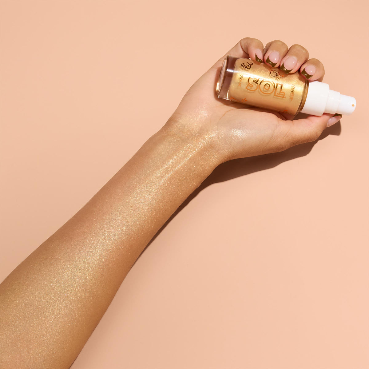 Hand holds a clear glass bottle with white pump of ColourPop SOL Glow Oil, It’s a Wolf Thing, while the golden oil is swatched along the forearm, revealing a luminous, sun-kissed sheen against a peach background.