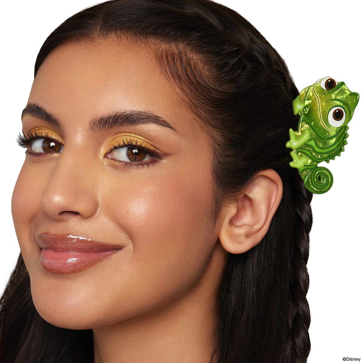 Smiling woman wearing shimmery gold eyeshadow and glossy lips from the Disney Tangled and ColourPop Collection full collection set, with a green Pascal chameleon hair clip accent, promoting Colourpop favorite now Back In Stock.