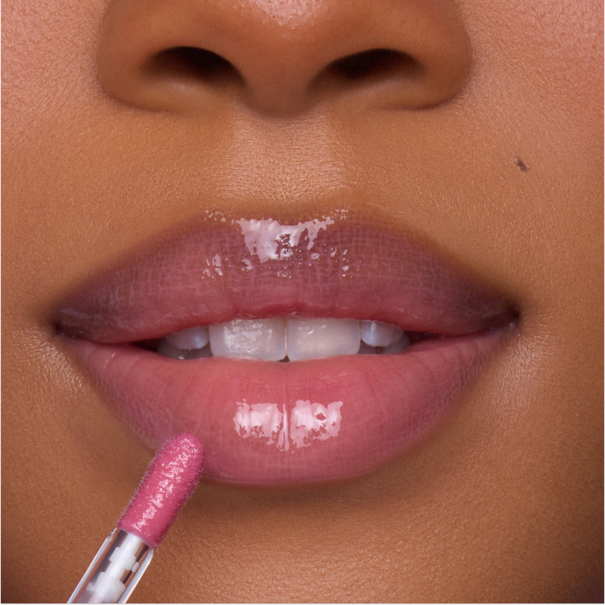 Close-up of a model applying Heart to Get Your New Obsession Ultra Glossy Lip, a high-shine pink lip gloss, with a doe-foot applicator on smooth, full lips for a juicy, plumped finish.