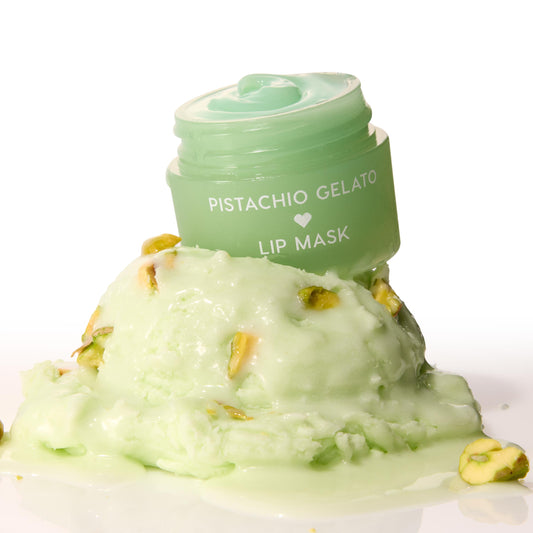 Mint-green Pistachio Gelato lip mask jar, lid off to reveal glossy balm, perched on a melting scoop of pistachio gelato with nut pieces on a white background - ColourPop Lip Mask product shot emphasizing creamy texture and dessert-inspired scent.