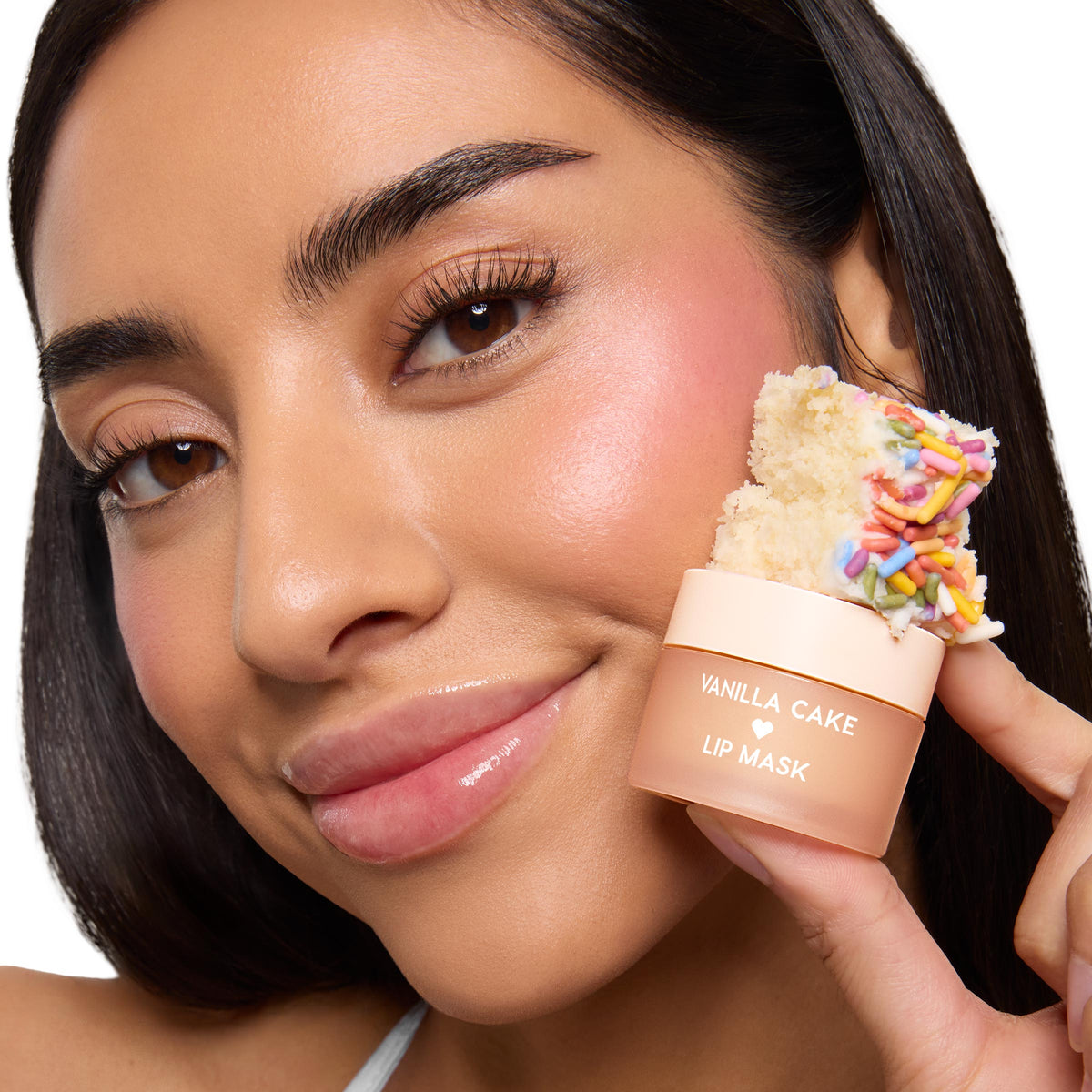 ColourPop Lip Mask jar in Vanilla Cake held beside a model’s glossy lips, highlighting hydration; peach pot labeled “Vanilla Cake Lip Mask” topped with a slice of vanilla cake and rainbow sprinkles in a clean studio close-up.